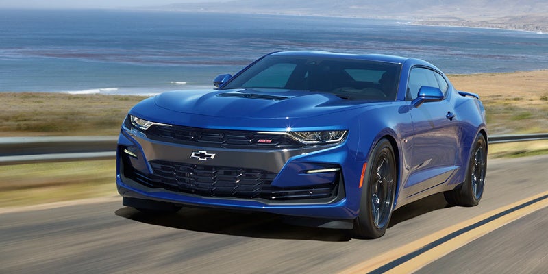 Blue Chevrolet Camaro driving on a coastal road with the ocean in the background.