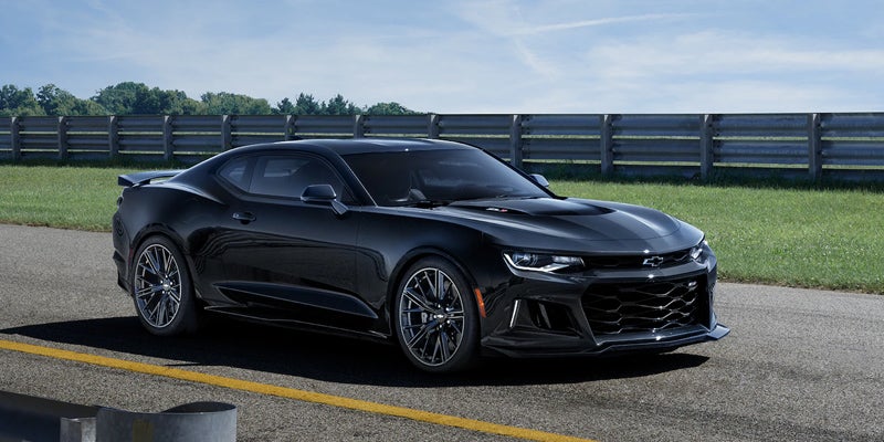 Black Chevrolet Camaro ZL1 parked on a race track with a barrier and grass in the background.