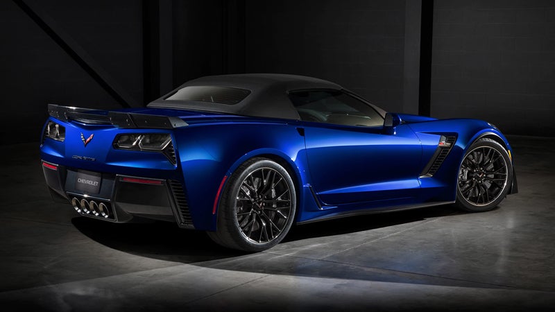 Blue Chevrolet Corvette convertible with a black soft top, viewed from the rear three-quarter angle in a dark setting.