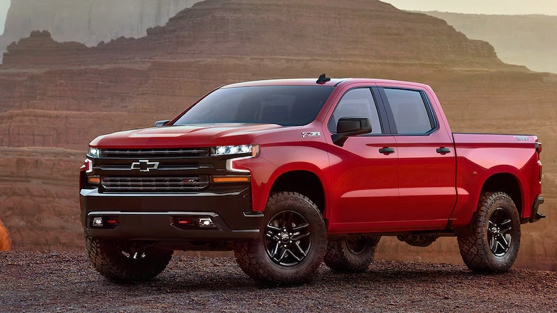 Red Chevrolet Silverado pickup truck with off-road tires parked in a desert landscape with mountains.