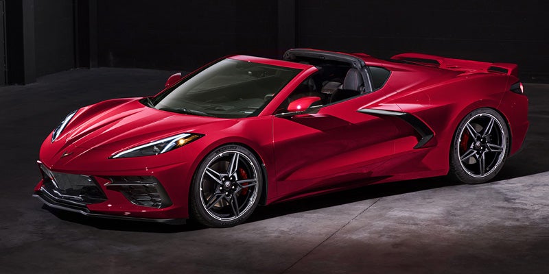 Red Chevrolet Corvette C8 convertible with its top down, parked in a dark garage.