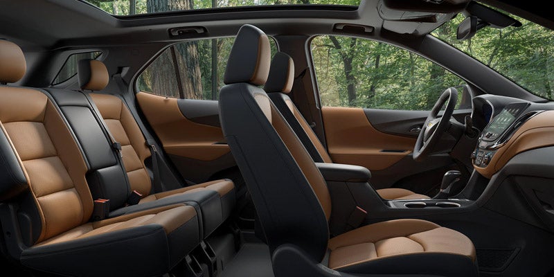 Car interior with two-tone tan and black seats, dashboard, sunroof, and trees visible through the windows