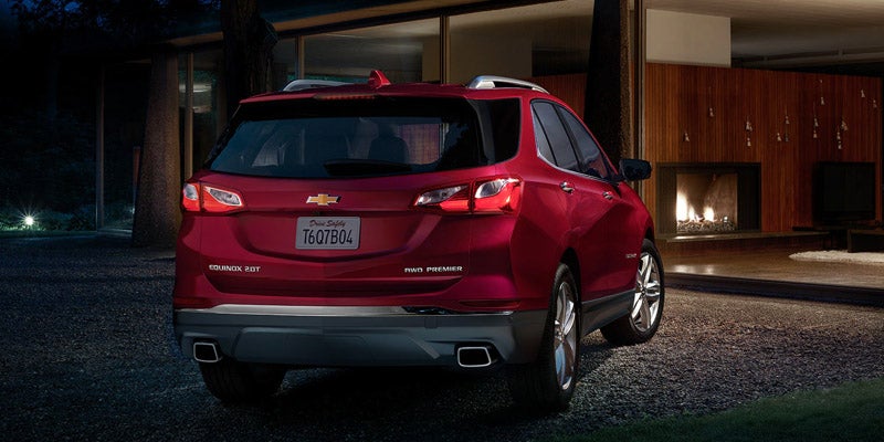 Red Chevrolet Equinox SUV parked at night in front of a modern house with a glowing fireplace.