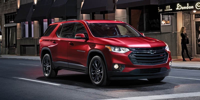 Red Chevrolet Traverse SUV parked on a city street at night, with illuminated buildings in the background.