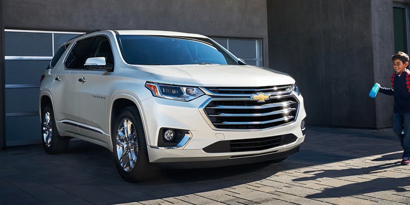 White Chevrolet Traverse parked in front of a garage, with a child holding a sponge nearby.