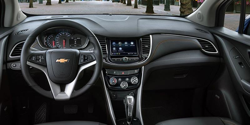Interior view of a dark gray car dashboard with a Chevrolet steering wheel, infotainment screen, and gear shifter.