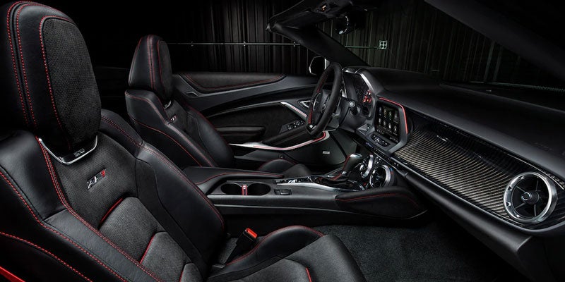 Black leather car interior with red stitching, carbon fiber dashboard trim, and a steering wheel.