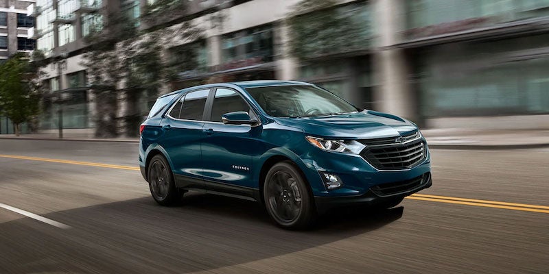 Dark teal Chevrolet Equinox SUV driving on a city street with motion blur.