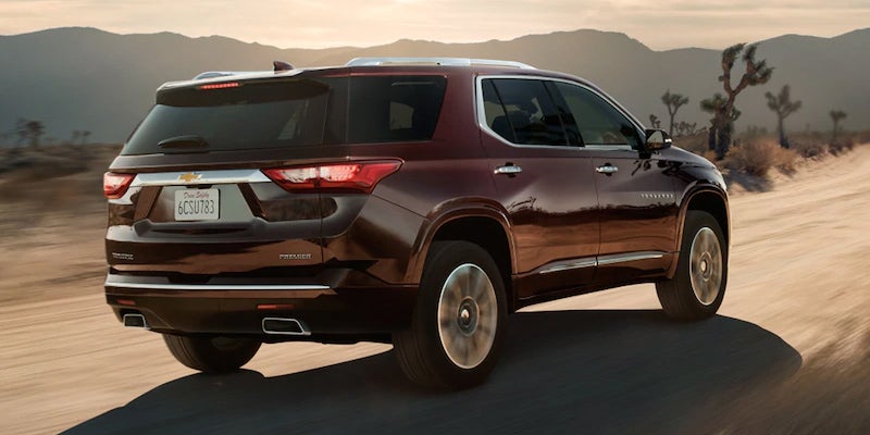 Dark red Chevrolet Traverse SUV driving on a dusty desert road at sunset.