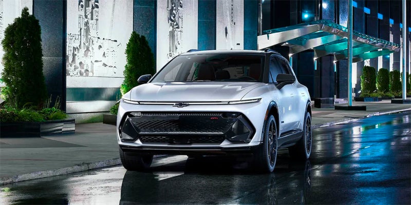 Silver Chevrolet Equinox EV parked on wet pavement in front of a modern building at night.