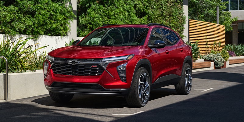 Red Chevrolet Trax SUV parked outdoors in front of a modern building with green landscaping.