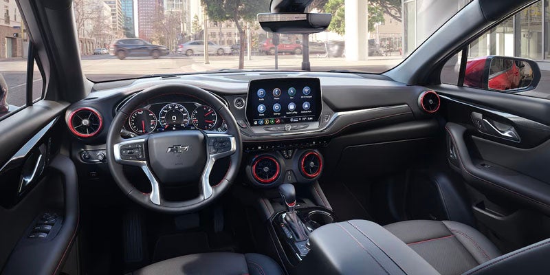 Car interior showing steering wheel, digital gauge cluster, infotainment screen, and red-accented vents.