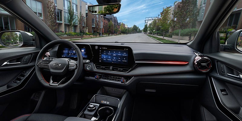 View from a car's driver seat showing the dashboard, steering wheel, and digital displays, with a city street outside.