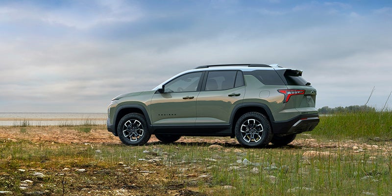 Green SUV with white roof parked on a grassy dirt path near water under a cloudy sky.
