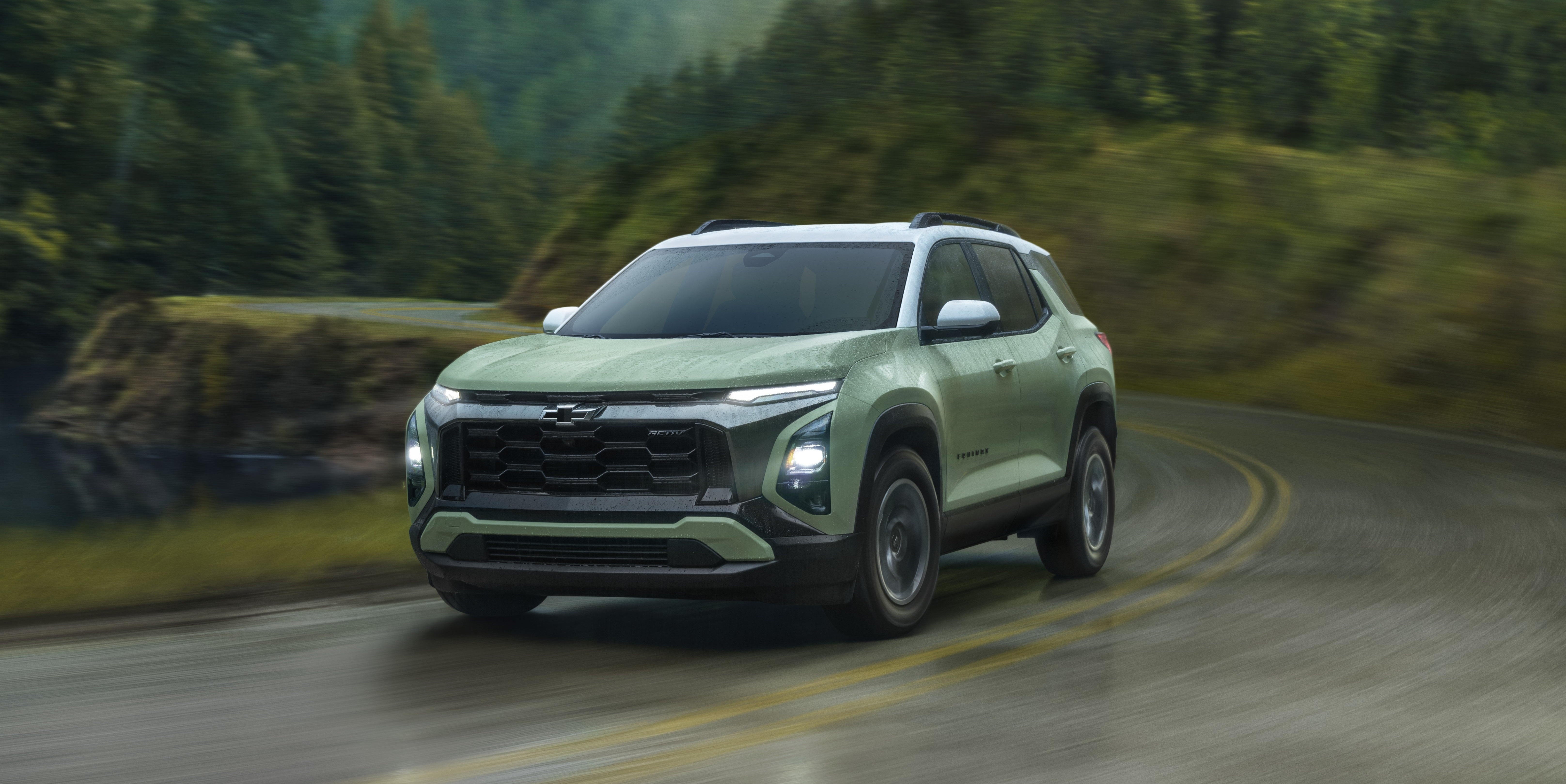 Light green SUV with white roof driving dynamically on a wet, winding road with blurred forest and mountains in the background.