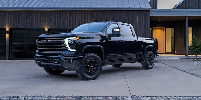 Black Chevrolet pickup truck parked on a concrete driveway in front of a modern dark wood house with garages.