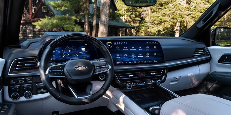 Car interior with black steering wheel, digital dashboard, and wide infotainment screen displaying app icons.