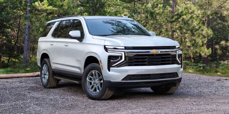 White Chevrolet Tahoe SUV parked on a gravel path with pine trees in the background.