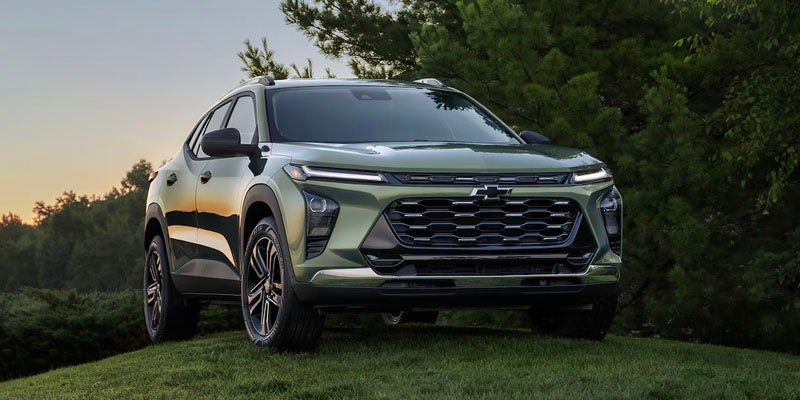 Front view of a green Chevrolet SUV parked on a grassy hill with trees and a light sky in the background.