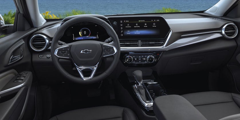 Modern car interior with black steering wheel, digital dashboard, large infotainment screen, and gear shifter.