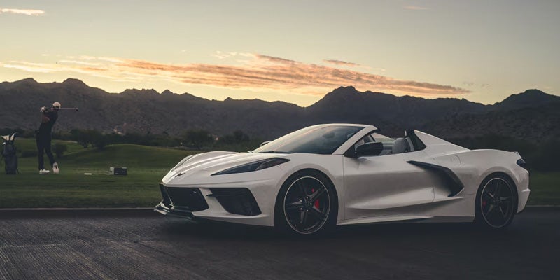 White convertible sports car parked outdoors with mountains and a sunset sky in the background