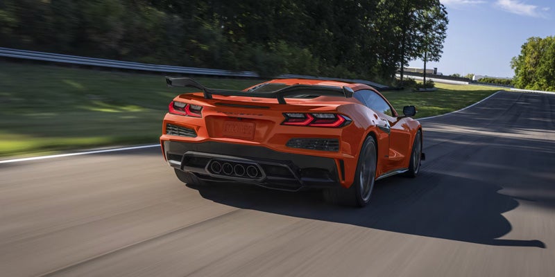Orange Chevrolet Corvette driving on a scenic road bordered by trees