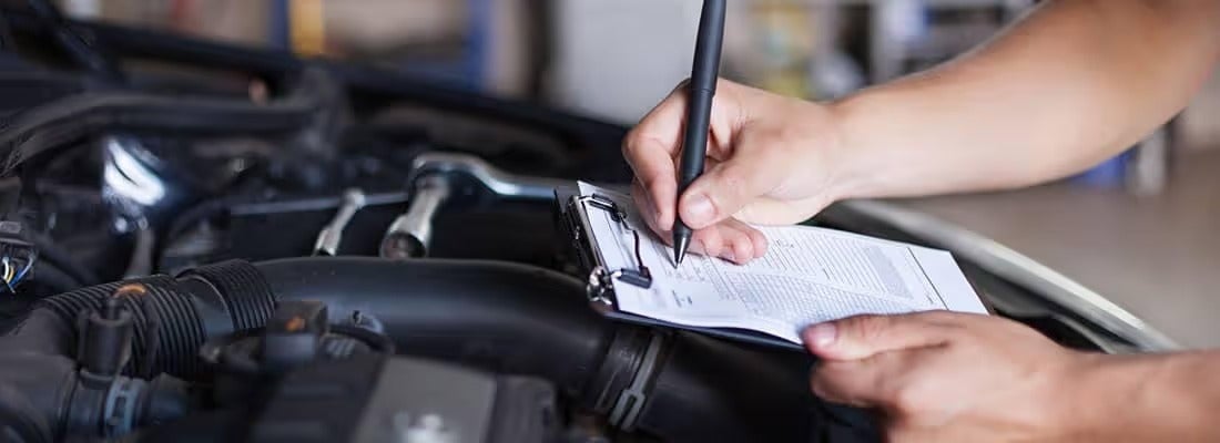 Auto mechanic filling out inspection checklist near engine
