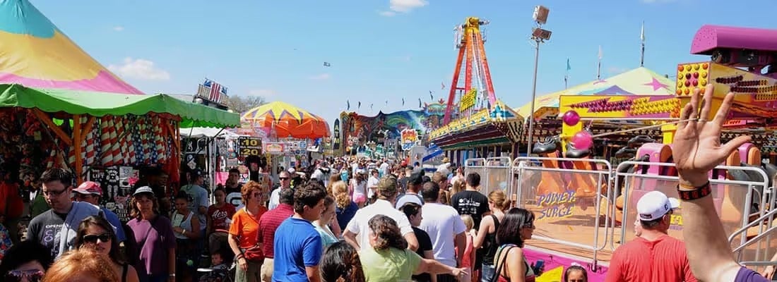 Crowded outdoor carnival midway with rides and tents