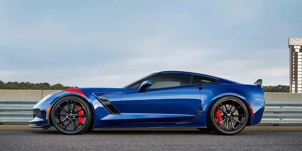 Blue Corvette sports car with a red fender stripe and red brake calipers, viewed in profile on a racetrack.