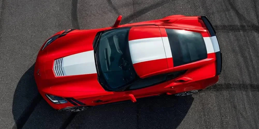 Aerial view of a red sports car with white racing stripes on an asphalt surface with tire marks.