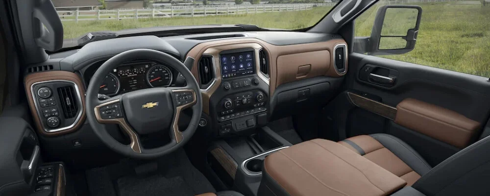 Interior of a Chevrolet truck with a black and brown dashboard, steering wheel, infotainment screen, and front passenger seat.