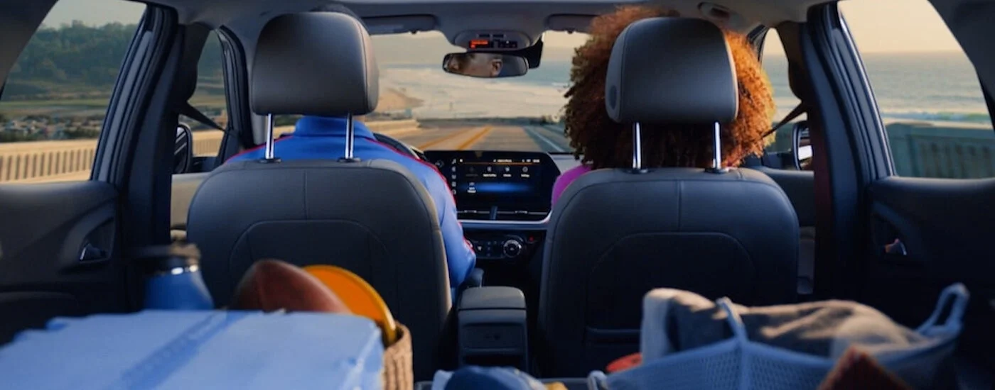 View from car's back seat of two people driving on a coastal road towards the ocean at sunset.